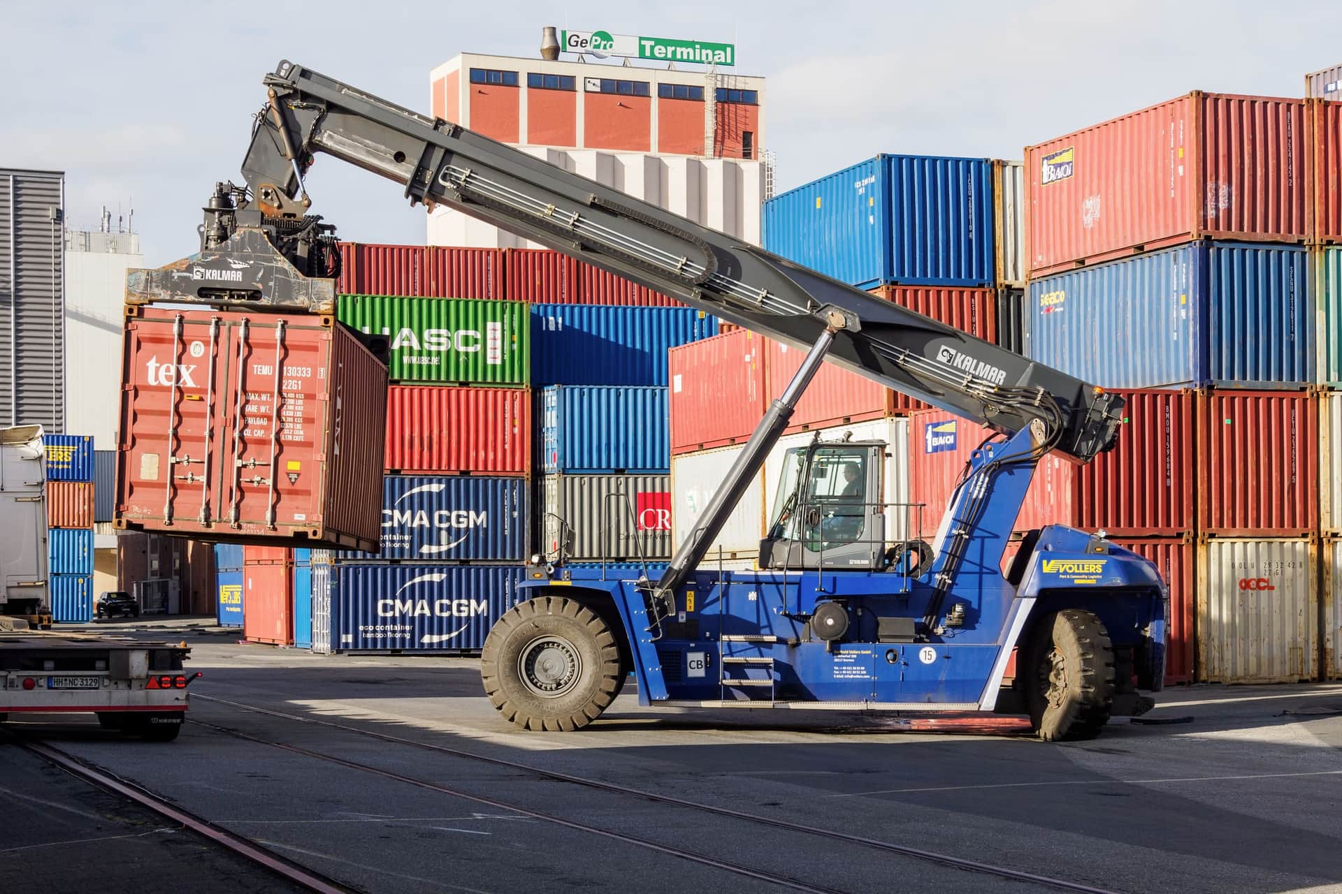 A reach stacker lifting a 20-foot container in front of stacked boxes at a depot in Bremen