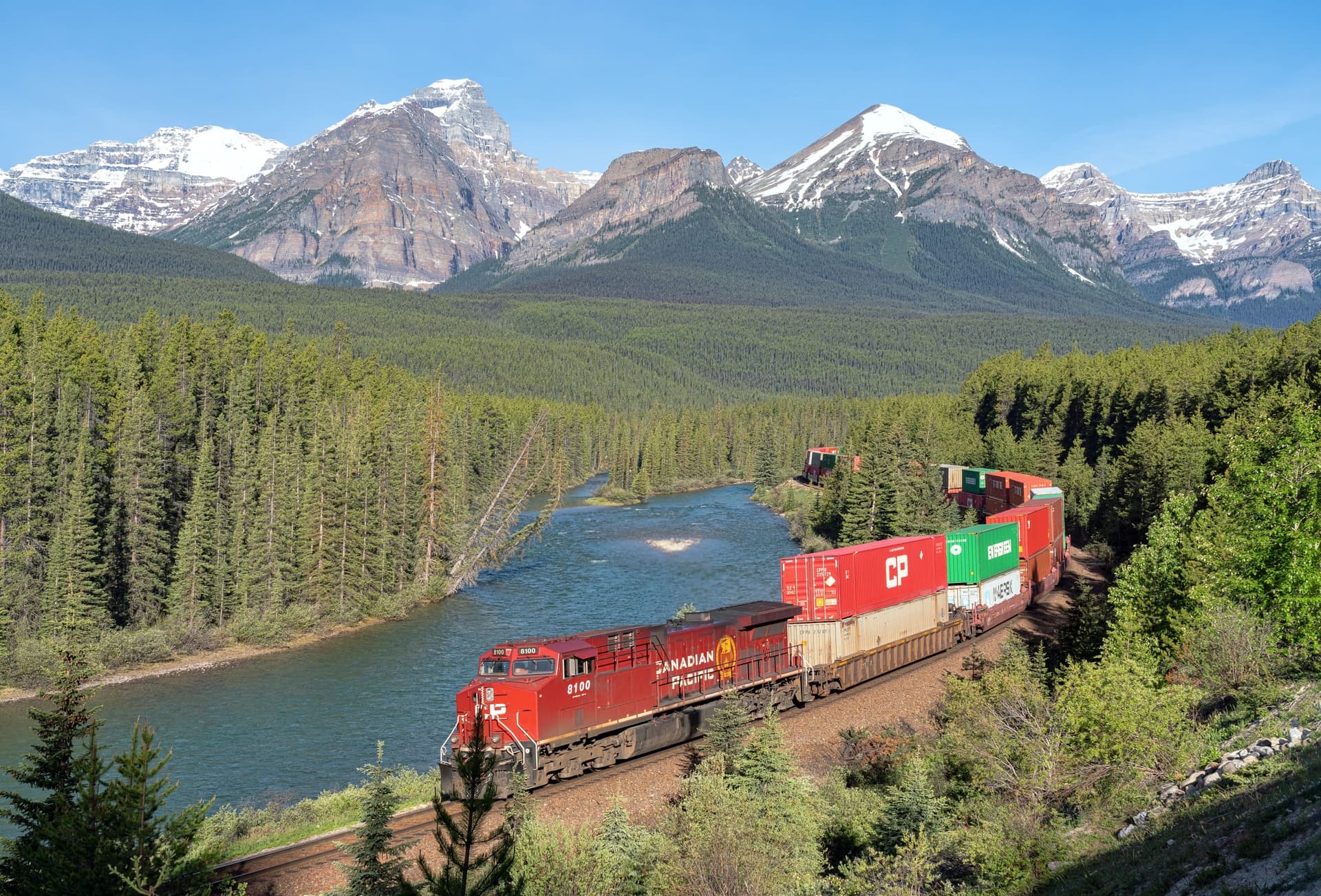 A double-stack container train rounding a river bend in the Canadian Rockies